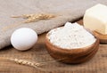 Wheat flour in a wooden bowl, butter and a whole egg on a wooden table.