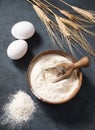 Wheat flour in a wooden bowl with a scoop on a dark blue background with eggs and dry branches wheat. Organic ingredients for Royalty Free Stock Photo