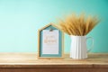 Wheat in vase and photo frame on wooden table over blue wall background. Shavuot holiday mock up for design