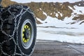 Wheel with black tire and mounted snow chains on the asphalt in front of the snow covered mountains in the high alps of Austria