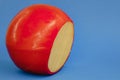 Wheel of fresh gouda cheese with a red rind on a blue monophonic background Royalty Free Stock Photo