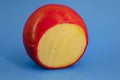 Wheel of fresh gouda cheese with a red rind on a blue monophonic background Royalty Free Stock Photo