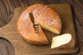 Cheese wheel and slice on a cutting board over a wooden table on Royalty Free Stock Photo