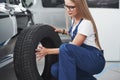 This wheel will fit perfectly. Nice blonde woman repairer is on her work. Indoors at car shop Royalty Free Stock Photo