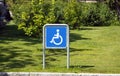 Wheelchair handicap sign in a parking against the backdrop of a green lawn.