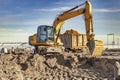 A wheeled excavator loads a dump truck with soil and sand. An excavator with a high-raised bucket against a cloudy sky View from Royalty Free Stock Photo