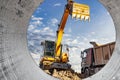 A wheeled excavator loads a dump truck with soil and sand. An excavator with a high-raised bucket against a cloudy sky View from Royalty Free Stock Photo