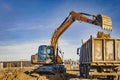 A wheeled excavator loads a dump truck with soil and sand. An excavator with a high-raised bucket against a cloudy sky View from Royalty Free Stock Photo