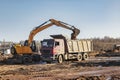 A wheeled excavator loads a dump truck with soil and sand. An excavator with a high-raised bucket against a cloudy sky View from Royalty Free Stock Photo