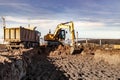 A wheeled excavator loads a dump truck with soil and sand. An excavator with a high-raised bucket against a cloudy sky View from