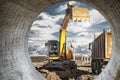 A wheeled excavator loads a dump truck with soil and sand. An excavator with a high-raised bucket against a cloudy sky View from