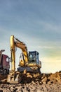 A wheeled excavator loads a dump truck with soil and sand. An excavator with a high-raised bucket against a cloudy sky View from Royalty Free Stock Photo