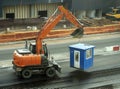 A wheeled excavator transports a booth. The excavator is driving through the construction site.