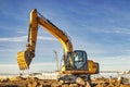 A wheeled excavator in a trench digs the ground. An excavator with a highly raised bucket against a cloudy sky. Earthworks at the Royalty Free Stock Photo