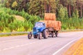 A wheeled tractor with a trailer with hay rides on the road. Royalty Free Stock Photo