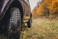 Wheels of an SUV on wet, fading grass at the edge of a forest in the Russian outback on a cloudy autumn day