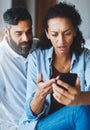 Where did all our money go. a dismayed couple receiving bad news via a smartphone at home.