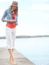 This is where I go to think...A happy young woman standing on a pier next to a lake.