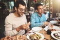 Where shall I start. two cheerful young men seated at a table eating pizza inside of a restaurant during the day. Royalty Free Stock Photo