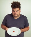 Wheres the rest of my burger. Portrait of an overweight man holding a plate with a tiny sliver of tomato.