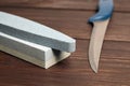 Whetstones and steel knife blade. Grindstones. Oval and rectangular double layer sharpening stone on wooden table background Royalty Free Stock Photo