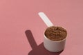 Whey Protein. Hard lighting and shadow. White scoop with chocolate flavour powder. Solid color, brown table. Royalty Free Stock Photo