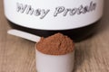 Whey Protein. White scoop with chocolate flavour powder and black jar. Wooden table. Close up, texture Royalty Free Stock Photo