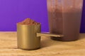 Whey Protein. Front view of scoop with chocolate powder and shaker on rustic wooden table. Solid color: violet. Royalty Free Stock Photo