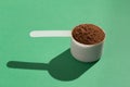 Whey Protein. Hard lighting and shadow. White scoop with chocolate flavour powder. Solid color, green table. Royalty Free Stock Photo