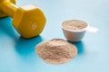 Whey protein powder in plastic measuring scoop near dumbbells on blue background Royalty Free Stock Photo