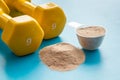 Whey protein powder in plastic measuring scoop near dumbbells on blue background Royalty Free Stock Photo