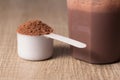 Whey Protein. White scoop with chocolate flavour powder and shaker. Wooden table. Close up, texture Royalty Free Stock Photo