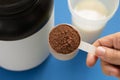 Whey Protein. Shaker with milk. Perspective, holding measuring scoop full of chocolate flavour powder on blue background Royalty Free Stock Photo