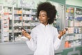 Which medicine is better, pharmacy, drug concept. Pretty African woman pharmacist or chemist choosing between two drugs Royalty Free Stock Photo