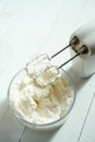 Whipped cream in a bowl and electric hand mixer on bright table. Royalty Free Stock Photo