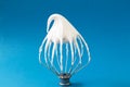Whipped egg whites - beaten italian meringue on a wire whisk on blue background, closeup and copy space