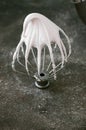 Whipped egg whites - beaten italian meringue on a wire whisk on gray background, copy space