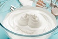 Whipped egg whites cream in glass bowl with whisks on blue wooden table.