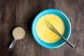 Whipped eggs in blue mixing bowl, metal whisk, measuring cup with raw quinoa, wood table