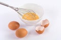 Whipped eggs in bowl with whisk and two egg and one broken on kitchen white table Royalty Free Stock Photo