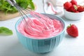 Whipping strawberry cream with balloon whisk on white wooden table, closeup