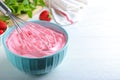 Whipping strawberry cream with balloon whisk on white wooden table, closeup. Space for text