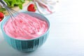 Whipping strawberry cream with balloon whisk on white wooden table, closeup. Space for text