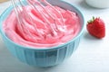 Whipping strawberry cream with balloon whisk on white wooden table, closeup
