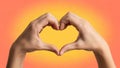 Hands forming a heart shape on vibrant orange background Royalty Free Stock Photo
