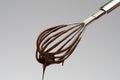 Whisk with liquid melted chocolate on light grey background Royalty Free Stock Photo