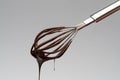 Whisk with liquid melted chocolate on light grey background Royalty Free Stock Photo