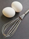 Two eggs and a whisk on a gray background, shot close up Royalty Free Stock Photo