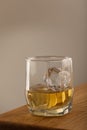 Whiskey or alcoholic beverage, with ie in a square formed designer glass. Sitting on an Oak table, with a backlighted gray surface