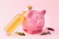 Whiskey bottle, piggy bank and plastic toy men on pink background, concept of alcoholism and drunkenness on last money